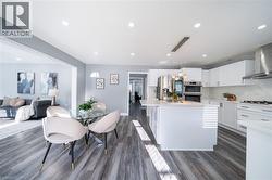 Modern kitchen featuring white cabinetry, stainless steel appliances, a center island with pendant lighting, and wood-finish flooring - 
