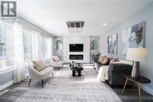 Bright living area featuring wood-finish flooring, a contemporary fireplace with a stone-look surround, and multiple windows with blinds - 151 Baldwin Drive, Cambridge, ON - Indoor Photo Showing Living Room With Fireplace