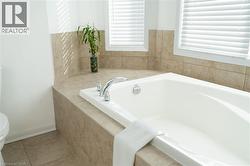 Soaking tub with chrome fixtures, surrounded by neutral-toned tiled decking and walls - 