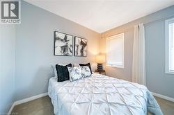 Bedroom featuring light blue walls, two windows with white blinds, and light-toned carpet flooring - 