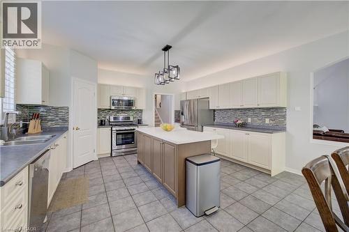 Kitchen featuring a central island with white countertop, stainless steel appliances, extensive white cabinetry, tile flooring, and a textured tile backsplash - 23 Buerkle Court, Kitchener, ON - Indoor Photo Showing Kitchen With Double Sink