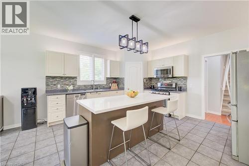 Kitchen featuring a central island with white countertop, recessed lighting, stainless steel appliances, white cabinetry, and tile flooring - 23 Buerkle Court, Kitchener, ON - Indoor