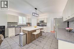 Kitchen featuring a central island with countertop seating, white cabinetry, stainless steel appliances, and a mosaic tile backsplash - 