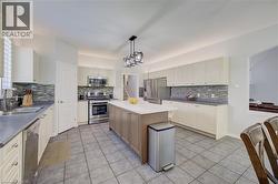 Kitchen featuring a central island with white countertop, stainless steel appliances, extensive white cabinetry, tile flooring, and a textured tile backsplash - 