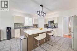 Kitchen featuring a central island with white countertop, recessed lighting, stainless steel appliances, white cabinetry, and tile flooring - 