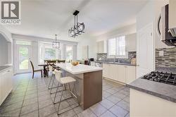 Open-concept kitchen and dining area featuring tile flooring, white cabinetry, a central island with a solid surface countertop, and modern pendant lighting - 