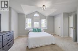 Room featuring vaulted ceiling, arched window, two rectangular windows with plantation shutters, ceiling-mounted light fixture, and carpet flooring - 