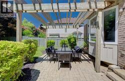 Pergola-covered patio featuring brick pavers, mature landscaping, wood fencing, and exterior brickwork - 