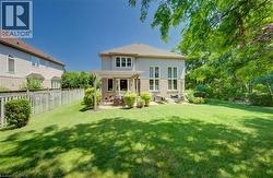 Expansive backyard featuring a large green lawn, a stone patio with a wood pergola, and mature trees providing natural screening - 