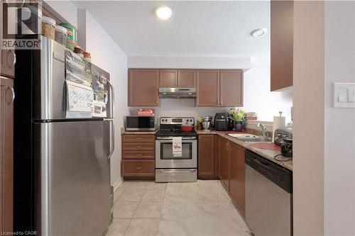 Kitchen with appliances with stainless steel finishes, a textured ceiling, under cabinet range hood, brown cabinets, and light marble finish flooring - 535 Margaret Street Unit# 74, Cambridge, ON 