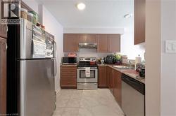 Kitchen with appliances with stainless steel finishes, a textured ceiling, under cabinet range hood, brown cabinets, and light marble finish flooring - 