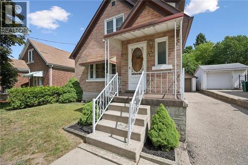 Brick exterior featuring a covered front porch with white railing, concrete steps, a paved driveway, and a detached two-car garage - 75 Arnold Street, Kitchener, ON - Outdoor With Facade