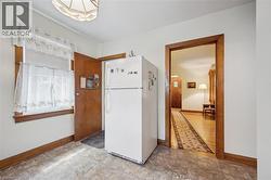 Light-filled room featuring durable flooring, a single window with wood trim, a paneled wood door, and a prominent white refrigerator - 