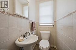 Pedestal sink with chrome-finish faucet, ceramic tile wainscoting with decorative border, flush-mounted toilet, and window with privacy blinds - 
