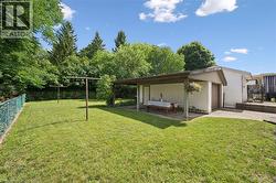 Spacious grassy yard featuring mature trees, a chain-link fence, and a covered patio area with an attached garage - 