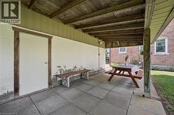 Covered patio area featuring concrete paver flooring, a wood beam ceiling, and a white exterior door with wood trim - 