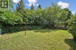 Expansive backyard featuring a lush lawn bordered by mature trees and natural stone retaining walls - 