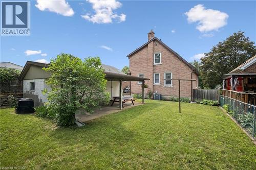 Expansive grassy yard area featuring a brick exterior structure, a covered patio with concrete flooring, and a separate outbuilding with block construction - 75 Arnold Street, Kitchener, ON - Outdoor