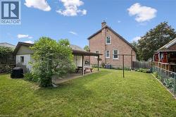 Expansive grassy yard area featuring a brick exterior structure, a covered patio with concrete flooring, and a separate outbuilding with block construction - 