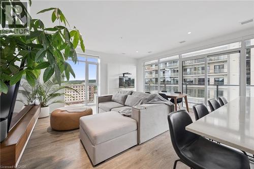 Open concept living area featuring wood-finish flooring, expansive floor-to-ceiling windows, recessed lighting, a built-in media console, and a large kitchen island with a light-colored countertop - 50 S Grand Avenue S Unit# 1002, Cambridge, ON - Indoor Photo Showing Living Room