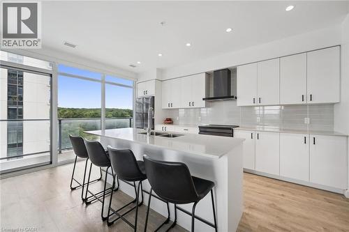 Modern kitchen featuring an expansive island with an integrated sink, sleek white cabinetry with black hardware, and wood-finish flooring - 50 S Grand Avenue S Unit# 1002, Cambridge, ON - Indoor