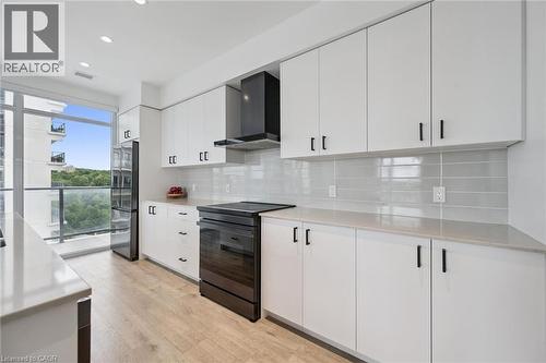 Modern kitchen featuring white cabinetry with black hardware, light wood-finish flooring, and light-toned countertops - 50 S Grand Avenue S Unit# 1002, Cambridge, ON - Indoor Photo Showing Kitchen