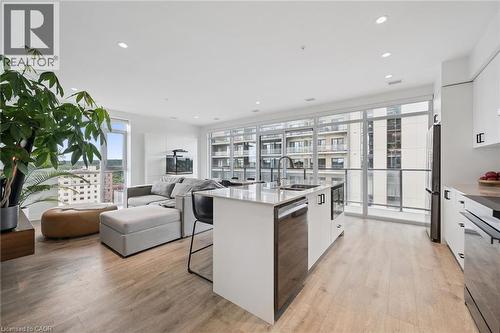 Open-concept living space featuring wood-finish flooring, a kitchen island with integrated sink, white cabinetry with dark hardware, and expansive floor-to-ceiling windows with balcony access - 50 S Grand Avenue S Unit# 1002, Cambridge, ON - Indoor
