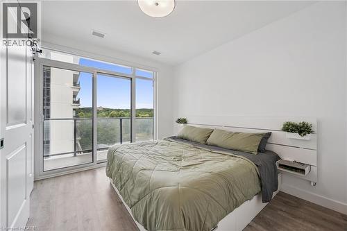 Room featuring a large sliding glass door with a balcony, wood-finish flooring, and a white ceiling light fixture - 50 S Grand Avenue S Unit# 1002, Cambridge, ON - Indoor Photo Showing Bedroom