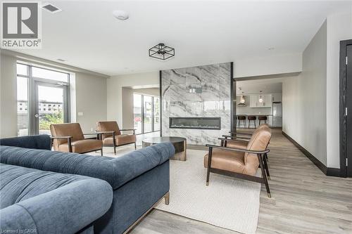 Spacious living area featuring a floor-to-ceiling marble-look fireplace with a linear insert, wood-finish flooring, large windows, and contemporary overhead lighting - 50 S Grand Avenue S Unit# 1002, Cambridge, ON - Indoor Photo Showing Living Room