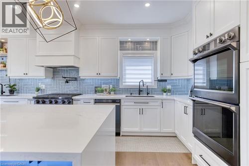 Kitchen featuring white shaker cabinetry, light blue herringbone tile backsplash, integrated stainless steel appliances, a center island with a light-toned countertop, and recessed lighting - 71 Ian Ormston Drive, Waterloo, ON 