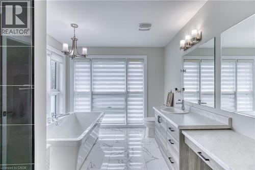 Spacious bathroom featuring a freestanding tub, dual-sink vanity with quartz-finish countertops, tiled flooring, and multiple windows with privacy blinds - 71 Ian Ormston Drive, Waterloo, ON 