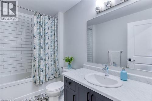 Bathroom featuring a white subway tile shower surround, a built-in tub, a dark wood-finish vanity with an integrated sink and light countertop, and patterned floor tile - 71 Ian Ormston Drive, Waterloo, ON 