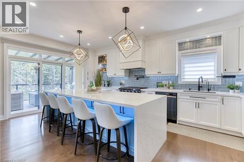 Spacious kitchen featuring a large central island with seating, white cabinetry, a light blue tiled backsplash, stainless steel appliances, and wood-finish flooring - 71 Ian Ormston Drive, Kitchener, ON - Indoor