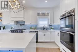 Kitchen featuring white shaker cabinetry, light blue herringbone tile backsplash, integrated stainless steel appliances, a center island with a light-toned countertop, and recessed lighting - 