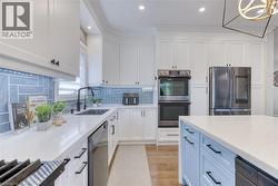 Modern kitchen featuring white cabinetry, a light blue tile backsplash, stainless steel double ovens, a stainless steel refrigerator, and a light blue kitchen island with a white countertop - 