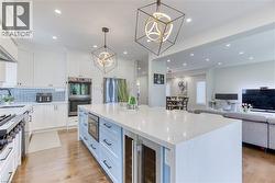 Modern kitchen featuring a large island with a light-colored countertop, integrated microwave, and beverage cooler - 