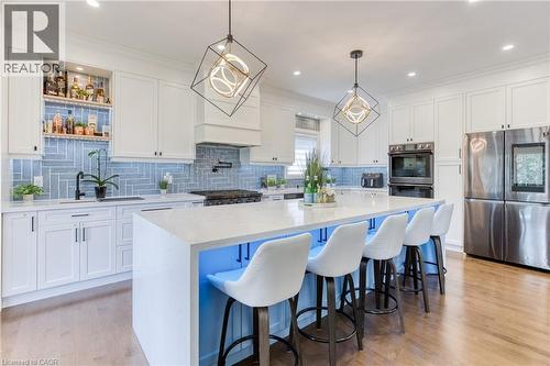 Gourmet kitchen featuring a large central island, light wood-finish flooring, white cabinetry, integrated stainless steel appliances, and a blue subway tile backsplash - 71 Ian Ormston Drive, Kitchener, ON - Indoor Photo Showing Kitchen With Upgraded Kitchen
