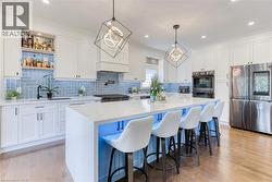 Gourmet kitchen featuring a large central island, light wood-finish flooring, white cabinetry, integrated stainless steel appliances, and a blue subway tile backsplash - 