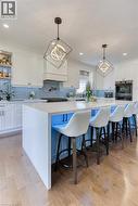 Kitchen featuring a large central island with seating, light wood-finish flooring, white cabinetry, a built-in oven, and a tile backsplash - 