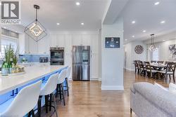 Spacious kitchen featuring white cabinetry, stainless steel appliances, a large island with seating, and wood-finish flooring - 