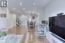Expansive open-concept living area featuring wood-finish flooring, recessed lighting, and a staircase with dark wood treads and a black railing system - 