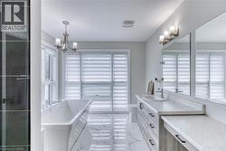 Spacious bathroom featuring a freestanding tub, dual-sink vanity with quartz-finish countertops, tiled flooring, and multiple windows with privacy blinds - 