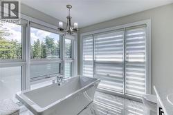 Freestanding soaking tub featuring chrome fixtures, surrounded by large windows with horizontal blinds, polished tile flooring, and a contemporary chandelier - 