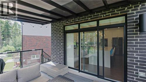 Covered outdoor patio with dark brick exterior and a clear glass railing - 71 Ian Ormston Drive, Kitchener, ON - Outdoor With Exterior