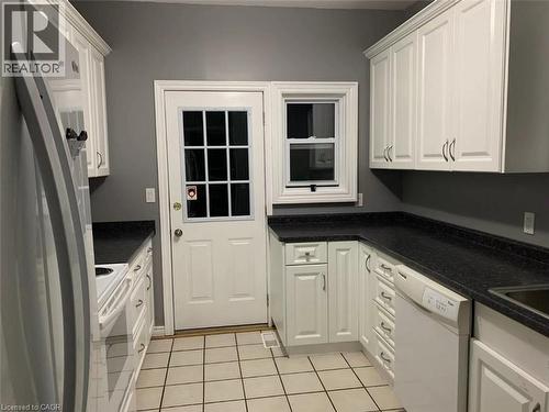 U-shaped kitchen with white cabinetry, dark countertops, tile flooring, a window, and an exterior door - 1066 Richmond Street, London, ON 