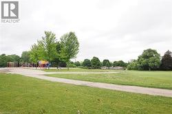 Expansive green space featuring a paved pathway, mature trees, and a distant recreational play structure - 