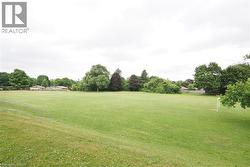 Expansive green space featuring a large grassy field, distant residential structures, and a perimeter of mature trees - 