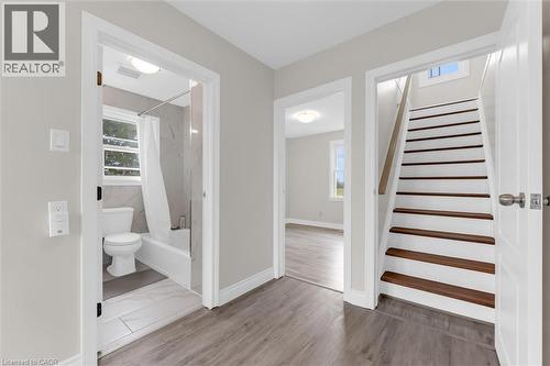 Hallway featuring wood-finish flooring, a full bathroom with tiled walls and flooring, and a staircase with wood treads and a contrasting white riser - 87 Mud Street E, Grimsby, ON 