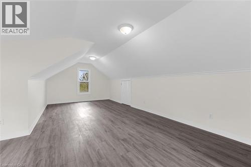 Spacious attic room featuring wood-finish flooring, a window offering natural light, and two ceiling-mounted light fixtures - 87 Mud Street E, Grimsby, ON 