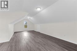 Spacious attic room featuring wood-finish flooring, a window offering natural light, and two ceiling-mounted light fixtures - 